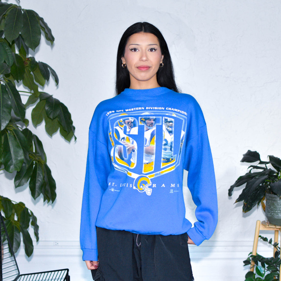 Model wearing a vintage crewneck sweatshirt from 1999 that has kurt warner, Marshall Faulk, and Isaac Bruce